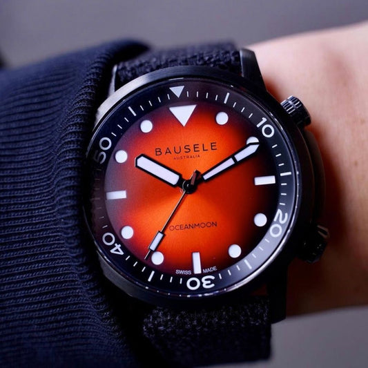 Close cropped photo of luxury waterproof Asutralian watch from Australian watch company. Dial has red and black background, orientation triangle at 12 and luminous hands.