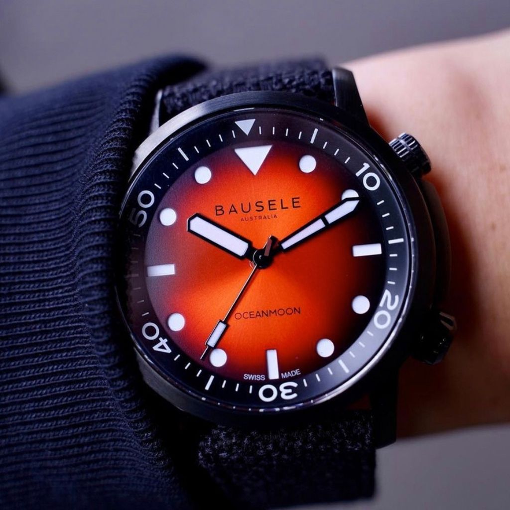 Close cropped photo of luxury waterproof Asutralian watch from Australian watch company. Dial has red and black background, orientation triangle at 12 and luminous hands. 